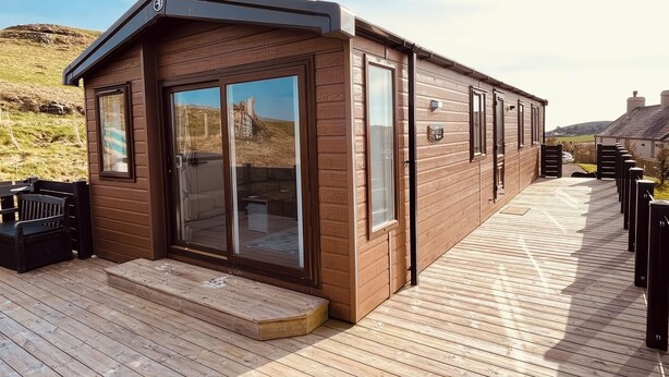 A wooden cabin with a deck, large sliding glass doors, and a sign reading "Lodge." - The Lodge at Pennant-igyn (Pwllheli)