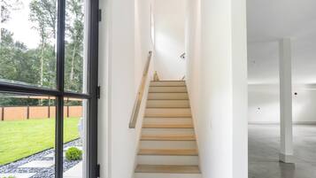 Un interior modern amb una escala que condueix a un segon pis, una finestra gran amb vista a un prat verd, i una habitació espaiosa i buida.