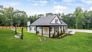 Une maison moderne à deux étages, dotée d’un porche abrité et entourée d’une pelouse bien entretenue et d’arbres.