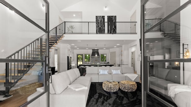 Un salon moderne avec un grand canapé d’angle, un tapis noir et deux petites tables d’appoint en osier.