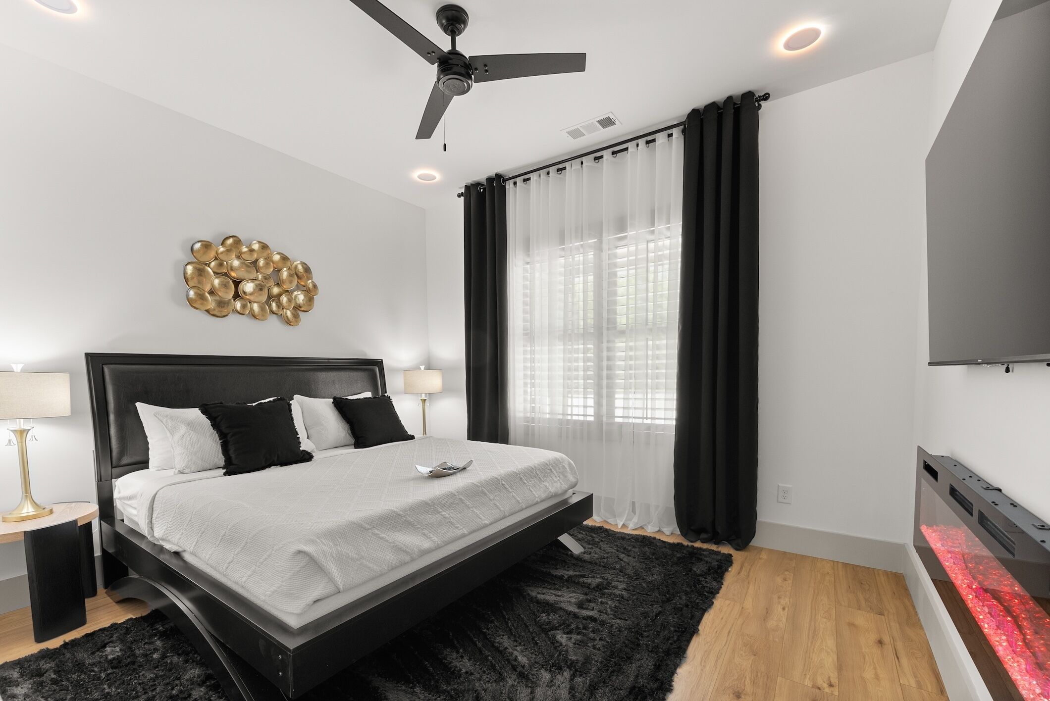 A modern bedroom with a bed, ceiling fan, and a wall-mounted TV.