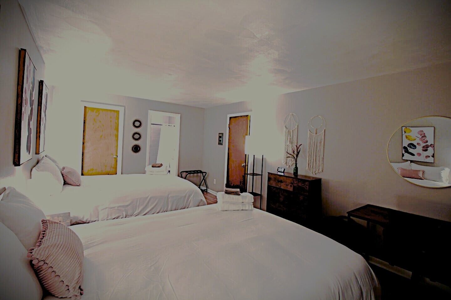 A bedroom with two beds, a dresser, a mirror, and wall art.