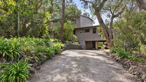 A modern two-story house with a gravel driveway leading to a wooden gate. - Golf Edge (Anglesea)