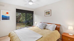 A bedroom with a bed, a nightstand, a lamp, a ceiling fan, and two framed pictures on the wall. - Golf Edge (Anglesea)