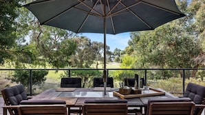 An outdoor patio with a table and chairs, an umbrella, and a view of a golf course. - Golf Edge (Anglesea)