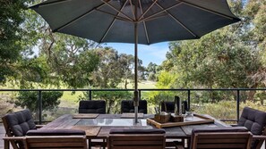 Un patio exterior con una mesa, sillas, un paraguas y vistas a un campo de golf.