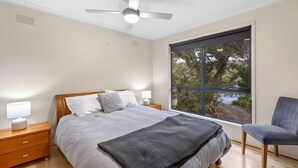 A bedroom with a bed, bedside tables, a chair, a window, and a ceiling fan. - Golf Edge (Anglesea)