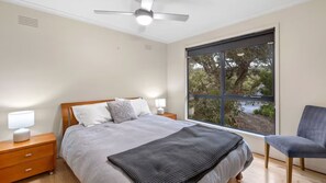 Un dormitorio con cama, mesitas de noche, una silla, ventana y ventilador de techo.