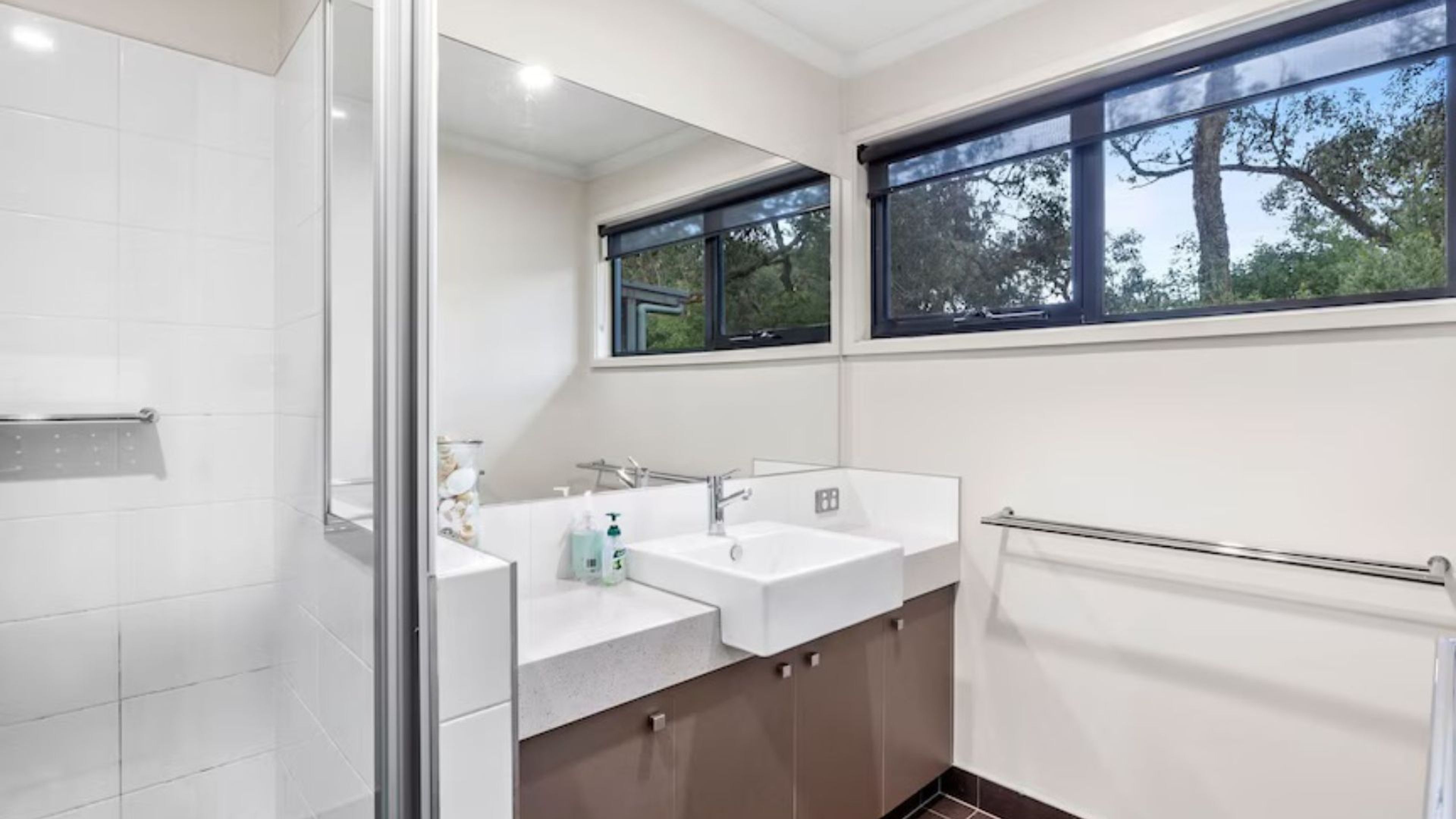 A modern bathroom with a glass shower enclosure, two sinks, and a window providing natural light.