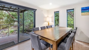 A modern dining area with a large wooden table, six grey upholstered chairs, and a floor lamp. - Golf Edge (Anglesea)
