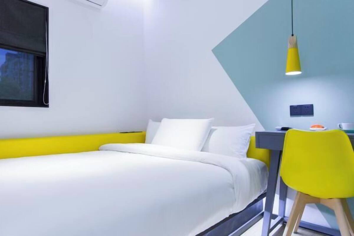 A modern hotel room with a bed, a desk, a chair, and a hanging light fixture.