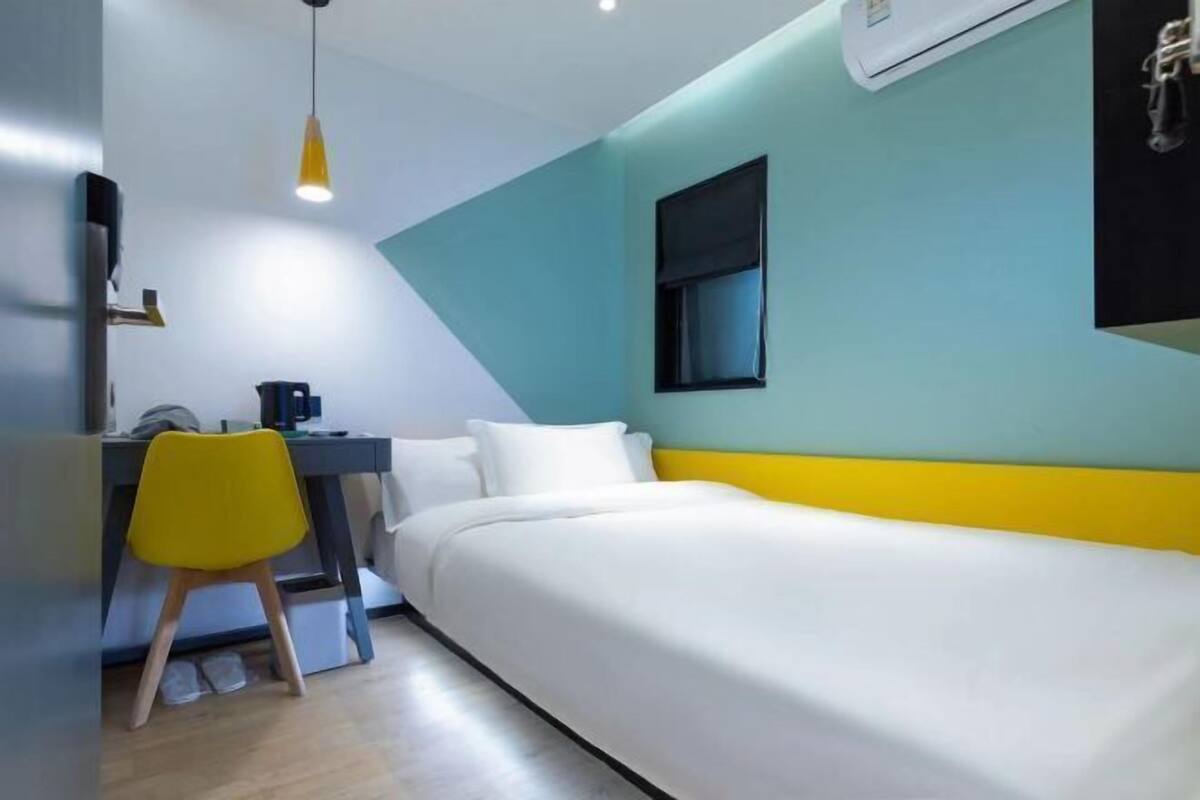 A small, modern room with a bed, a desk, a chair, and a window.