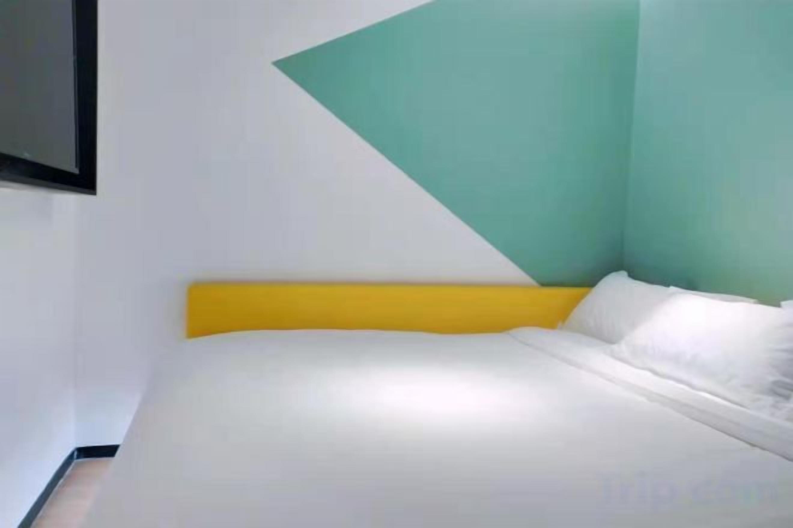 A bed with a yellow headboard in a room with teal and white walls.