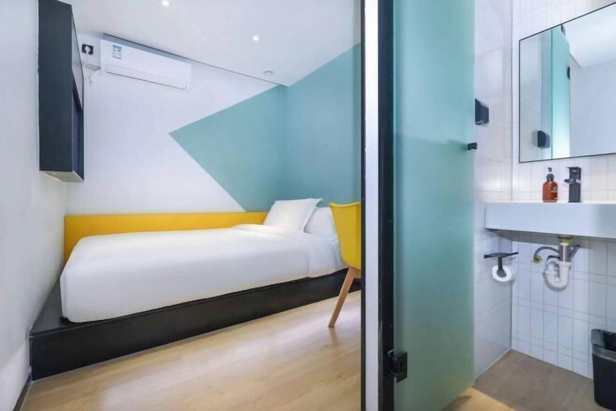 A modern hotel room with a bed, a bathroom with a sink and mirror, and a wall-mounted air conditioning unit.