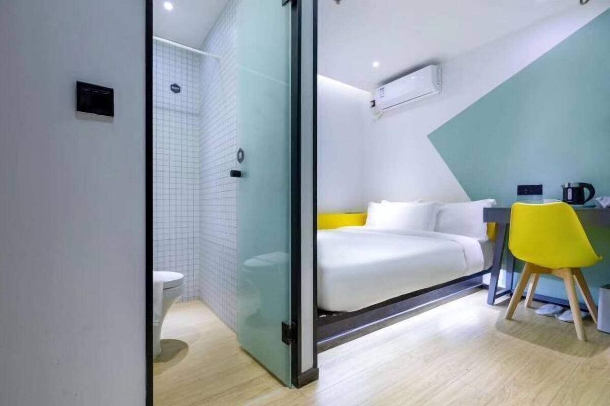 A modern hotel room with a glass partition separating the bathroom and bedroom.