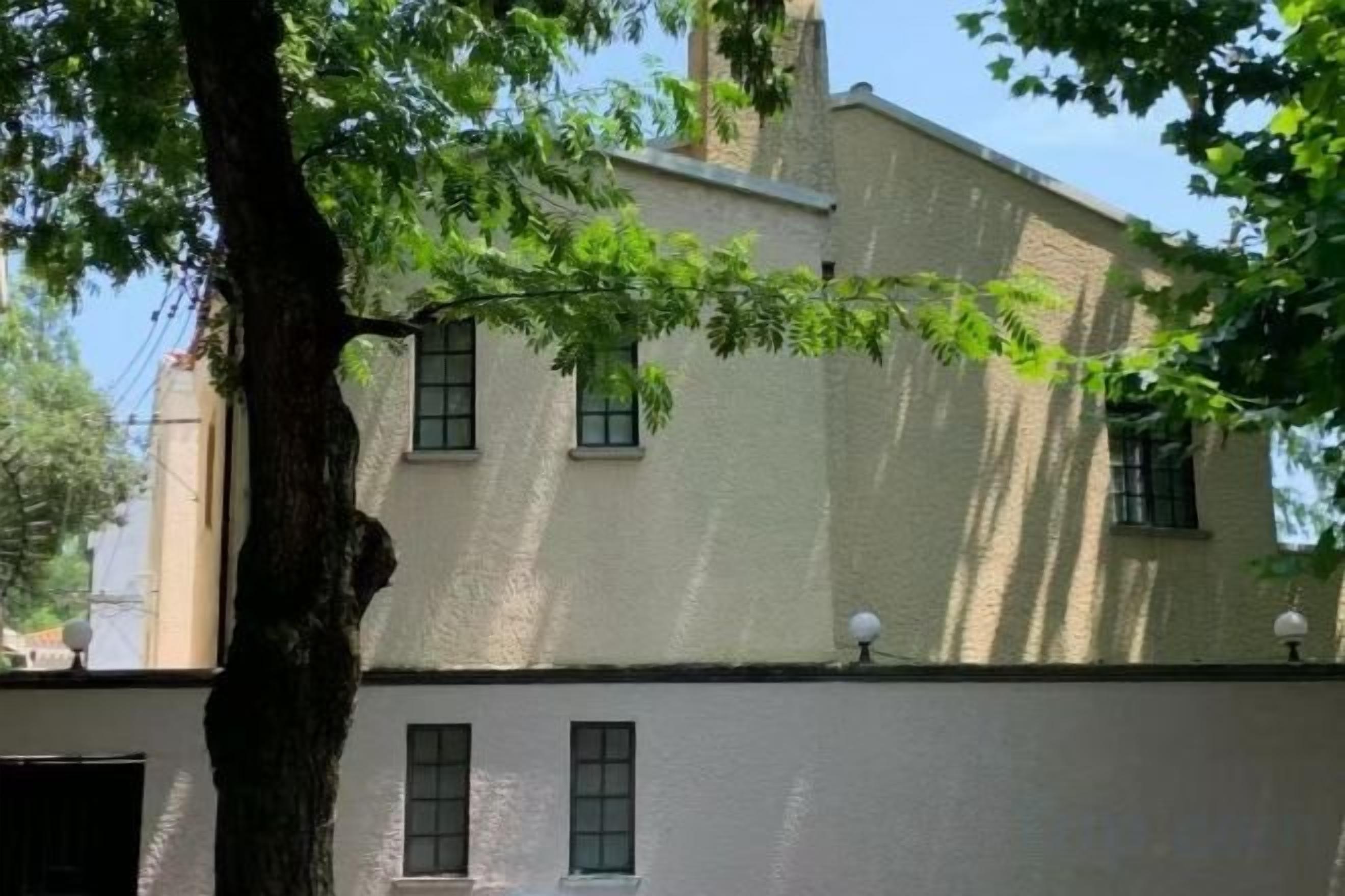 A building with a white facade, multiple windows, and a tree in the foreground.