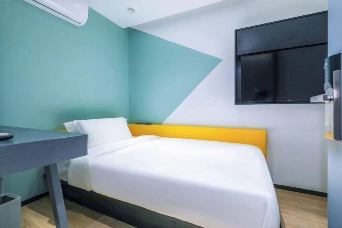 A hotel room with a bed, a desk, and a wall-mounted TV.