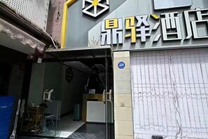 Entrada de hotel con una persiana cerrada, mostrador de recepción a la vista y un letrero con caracteres chinos.