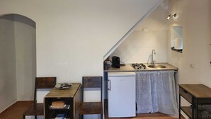 Una cocina compacta con un refrigerador blanco, un lavamanos y una pequeña zona de comedor con un banco y mesa.