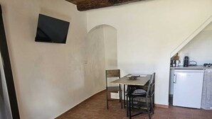 Una cocina compacta con una mesa de comedor, sillas, un refrigerador pequeño y un televisor fijado en la pared.