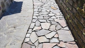 Un sendero de piedra atraviesa un patio con un muro de piedra a un lado y la entrada de un edificio al otro.