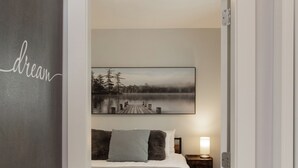 Un dormitorio con cama, mesita de noche, lámpara y un cuadro en la pared.