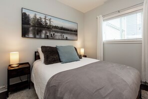 Une chambre à coucher avec un grand lit, deux tables de chevet avec des lampes, un tableau accroché au mur et une fenêtre avec des stores.