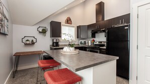 Una cocina moderna con una isla central, taburetes de bar, armarios oscuros y un refrigerador negro.