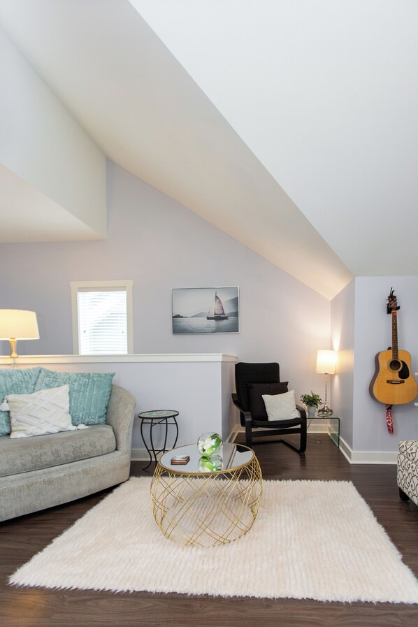 Un salon avec un canapé gris, un fauteuil noir, un tapis blanc, une table basse ronde et une guitare accrochée au mur.