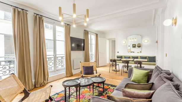 A modern living room with a grey sofa, wicker chair, and a dining area with a green sofa and chairs. - A PERFECT PARISIAN GETAWAY IN A PERFECT LOCATION – RUE DU TEMPLE (Paris)