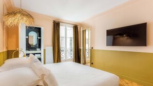 A hotel room with a bed, a TV, a bathroom with a mirror, and a balcony with curtains. - A PERFECT PARISIAN GETAWAY IN A PERFECT LOCATION – RUE DU TEMPLE (Paris)