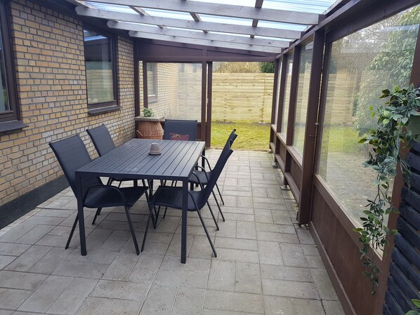 A patio with a table and chairs, a pergola, a brick wall, and a view of a wooden fence and grass.
