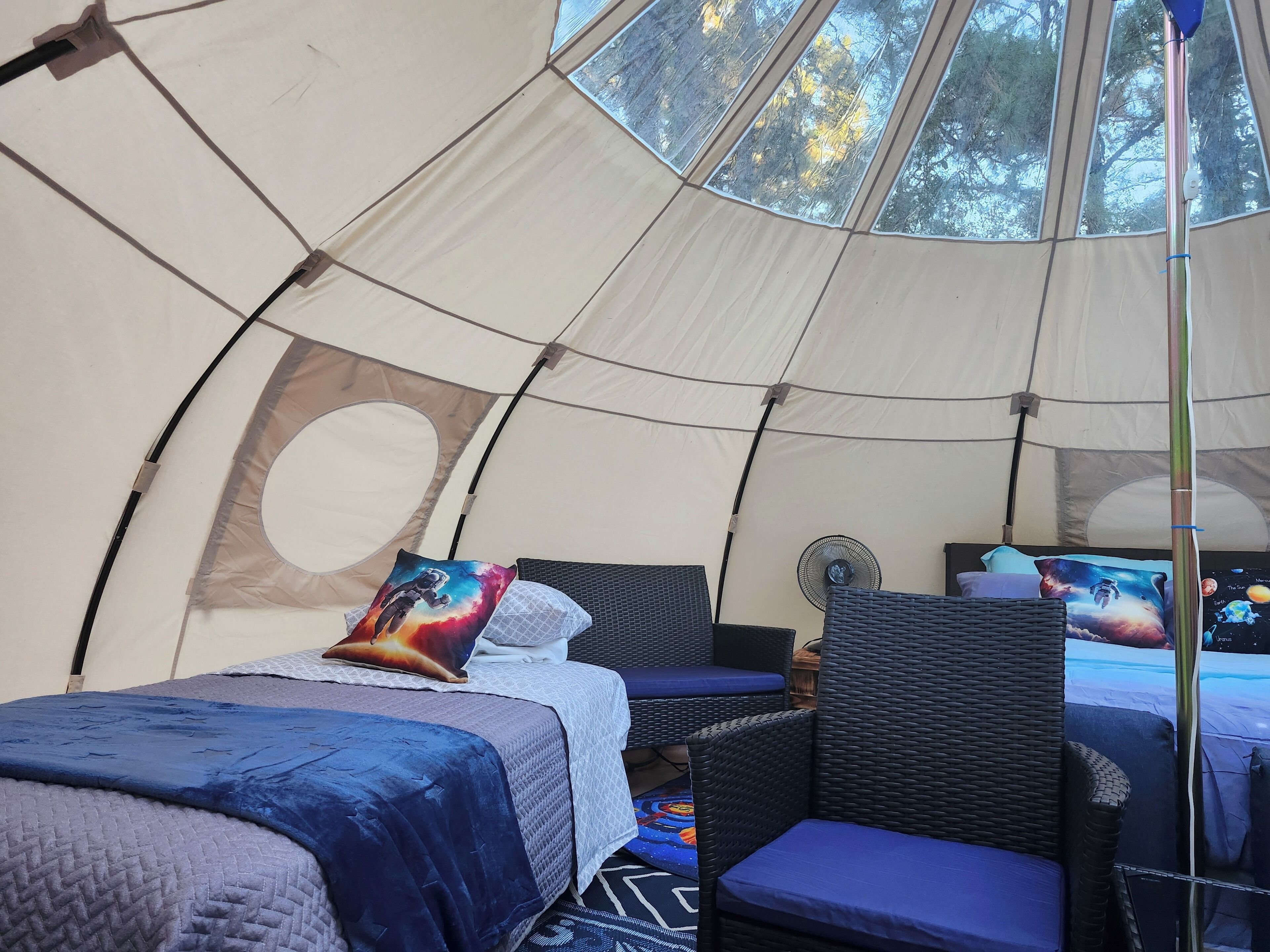 Una carpa con una cama, una silla y un ventilador.