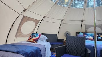 Una carpa con una cama, una silla y un ventilador.