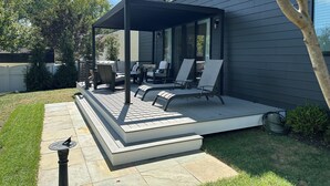 Eine überdachte Terrasse mit Gartenmöbeln, einem Vogelhaus und einem kleinen Garten.