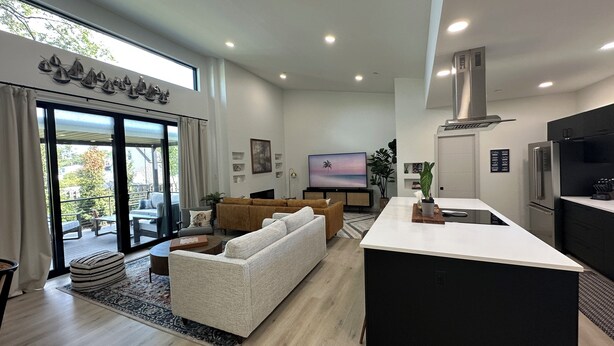 Eine moderne Küche mit einer zentralen Kochinsel, ein Essbereich mit einer Couch und ein Wohnzimmer mit Fernseher.