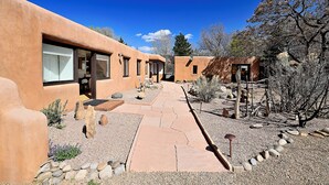 A modern building with a stucco exterior, a paved walkway, and a small garden area with rocks and sparse vegetation.
