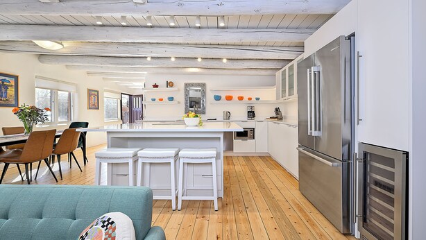 A modern kitchen with a central island, white bar stools, and stainless steel appliances.