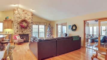 A spacious living room with a stone fireplace, a large sectional sofa, and a Christmas tree.