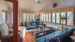 A cozy living room with a blue sofa, a coffee table, and a chair. There are large windows with curtains and a ceiling fan.