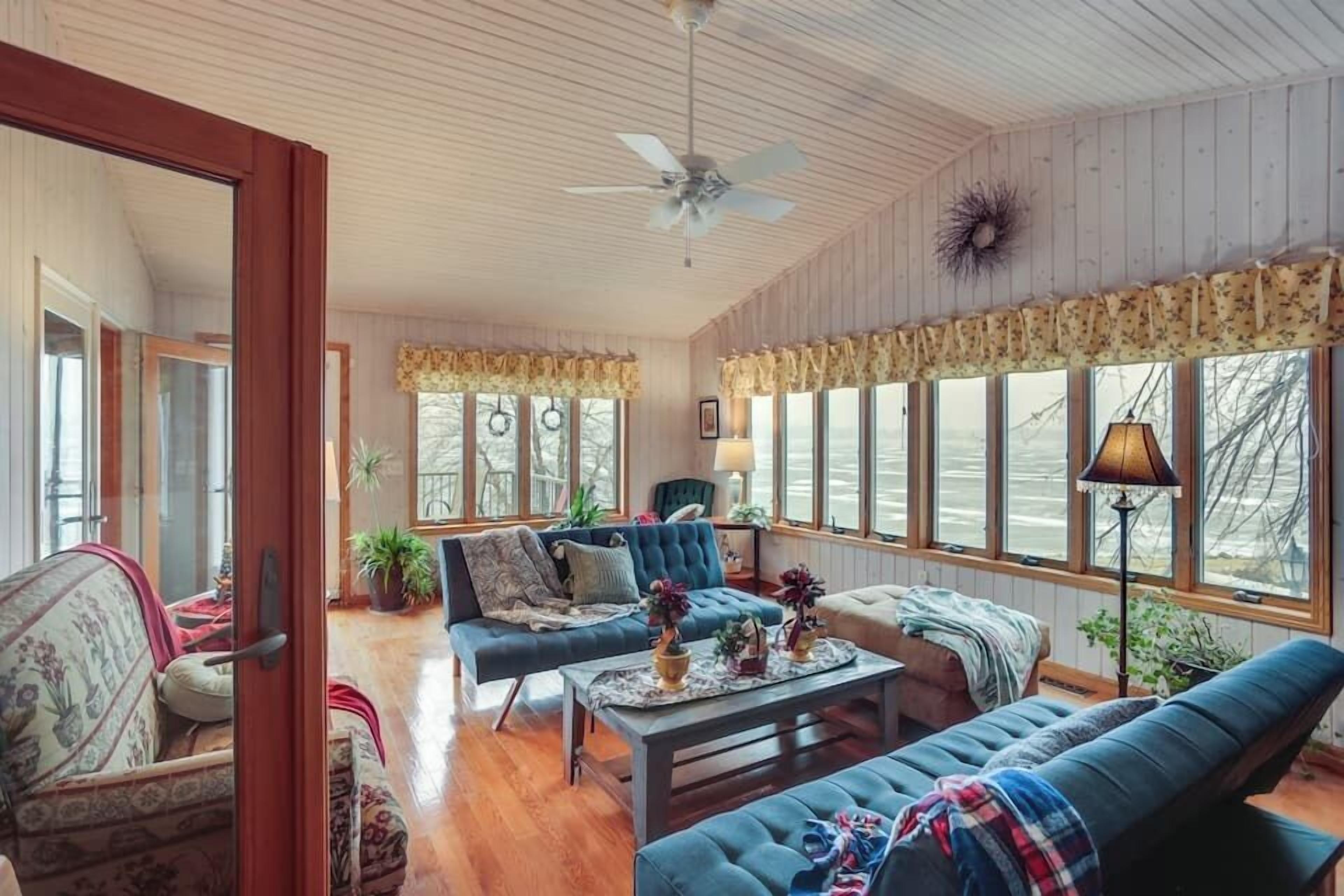 A spacious living room with a large window, a ceiling fan, and a fireplace.