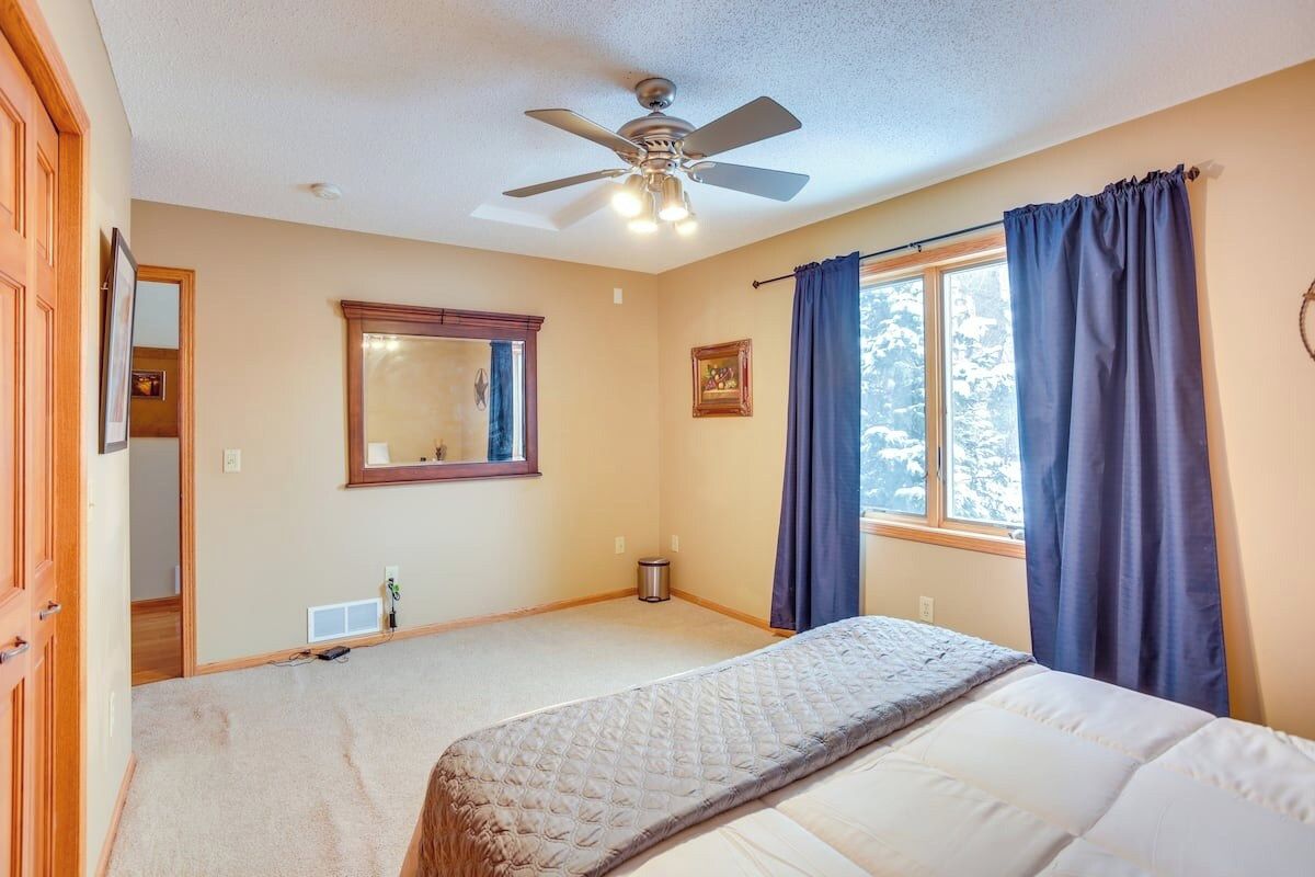 Un dormitorio con cama, ventilador de techo, ventana con cortinas y una puerta.