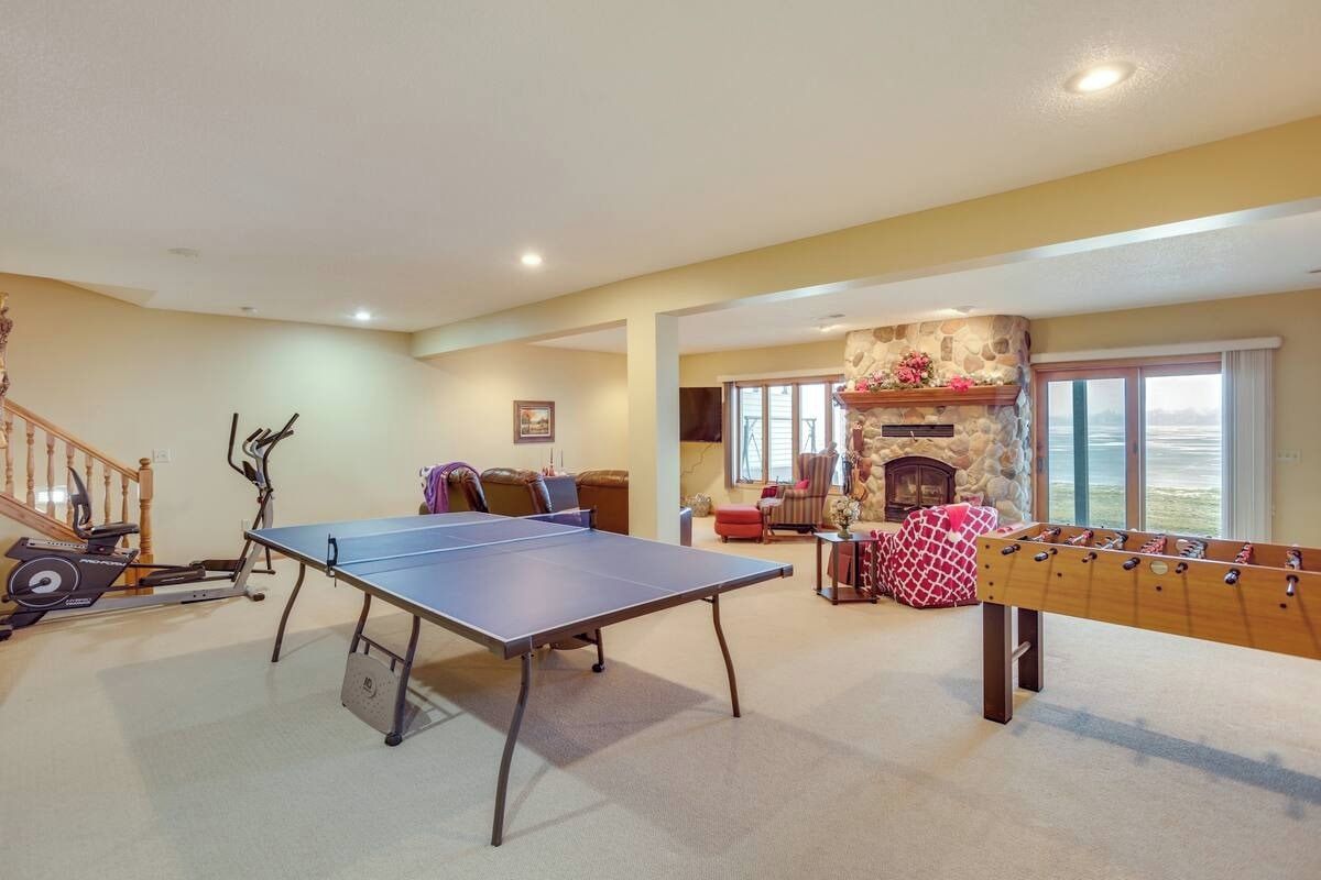 A room with a ping pong table, foosball table, exercise equipment, and a fireplace.