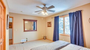 A bedroom with a bed, a ceiling fan, a window with curtains, and a mirror on the wall.