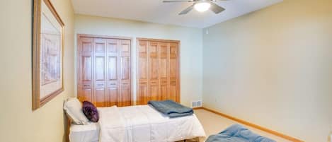 A bedroom with two beds, a ceiling fan, wooden wardrobes, and a framed picture on the wall.