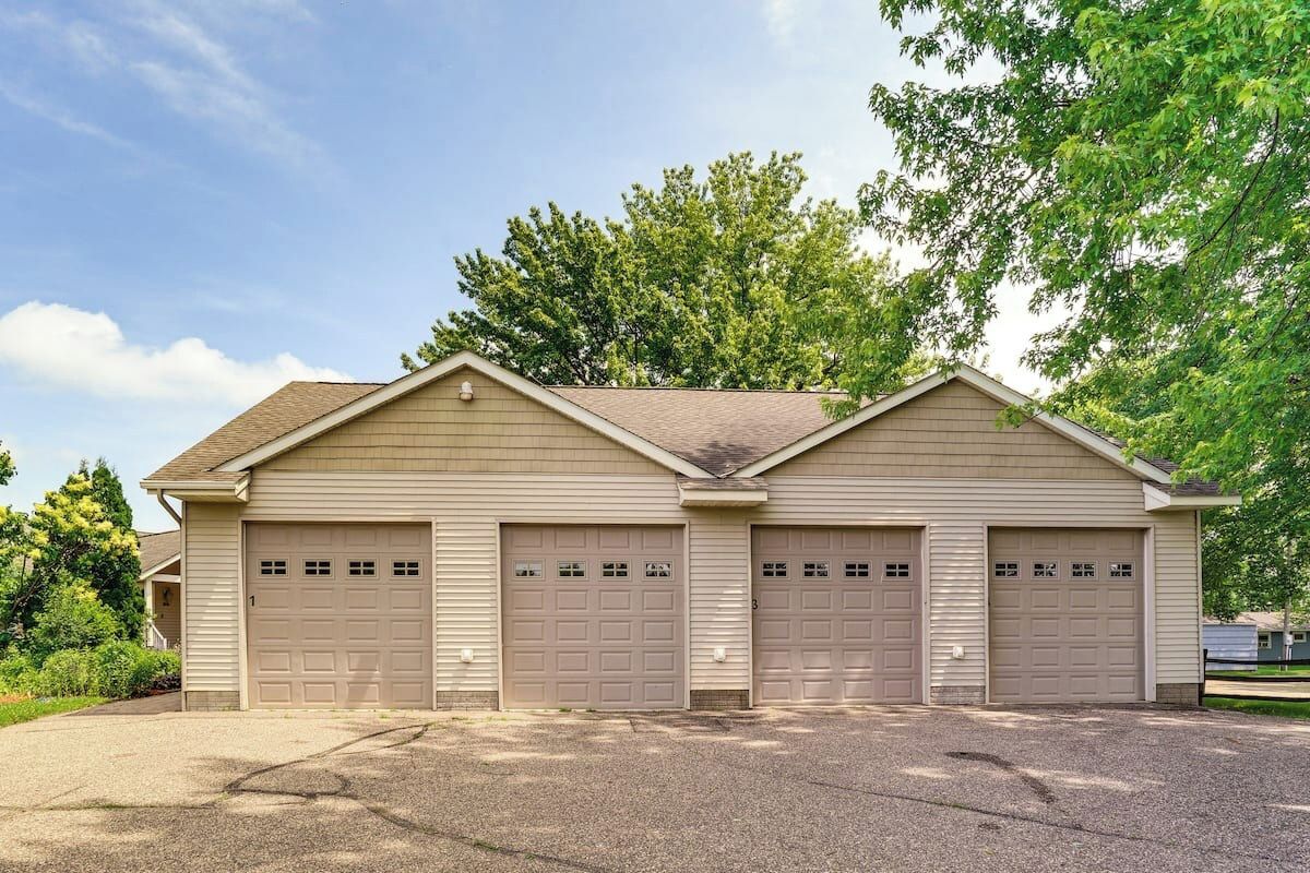A two-story building with three garage doors, a sloped roof, and a gravel driveway.