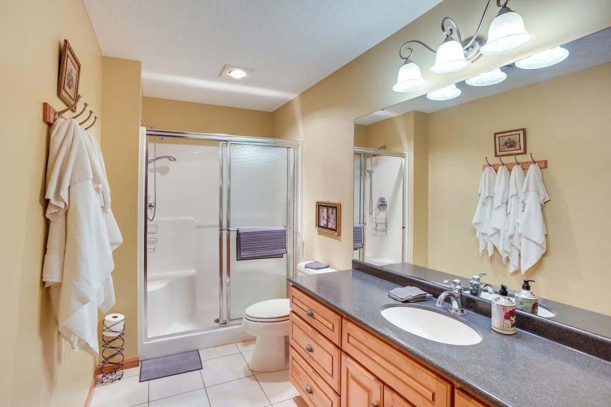 A bathroom with a shower, toilet, vanity with a sink, and a large mirror.