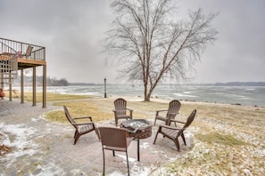Un patio con cuatro sillas Adirondack, un brasero y vista a un lago congelado.