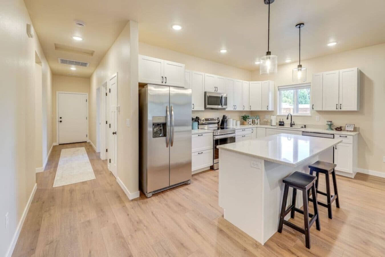 A modern kitchen with white cabinetry, stainless steel appliances, and a central island with bar stools.