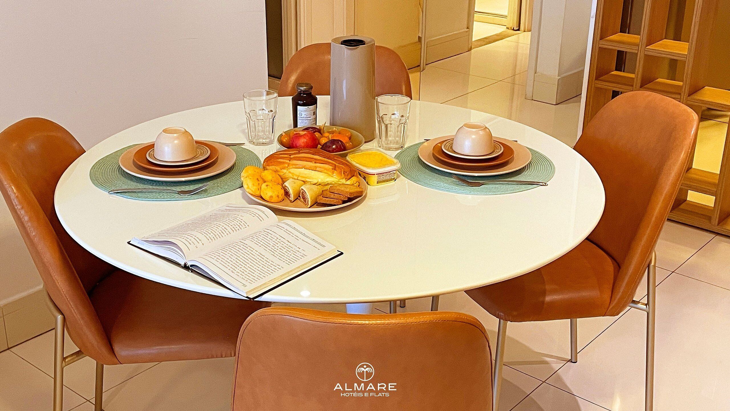 A round dining table with a book, a plate of food, and two cups.